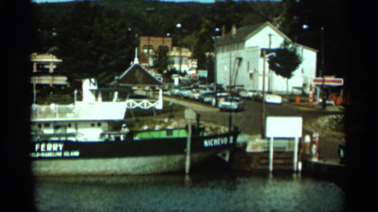 Ferry marked NICHEVO II near a pier, with cars and buildings along the shore.