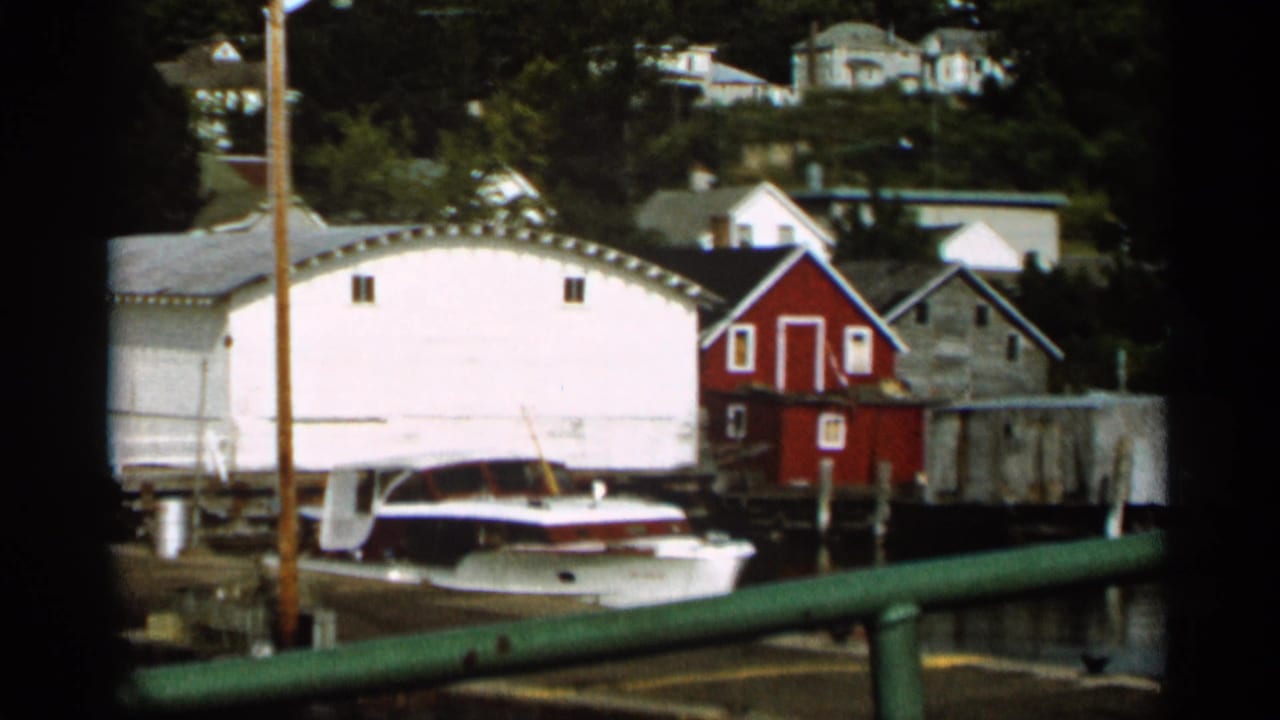 White boathouse and docked boat beside a red shed near the water.