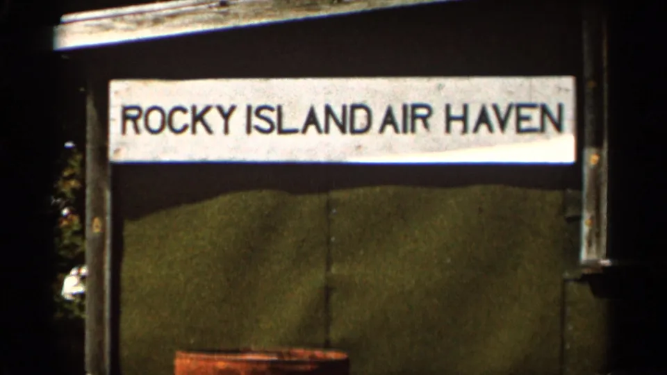 Handheld 8mm frame showing the Rocky Island Air Haven sign over green wall panels, with soft focus and faded color.