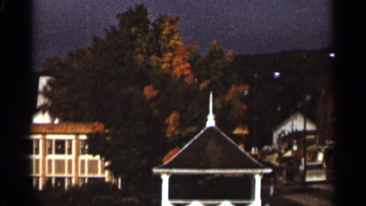 White gazebo and nearby buildings partly framed by autumn trees.