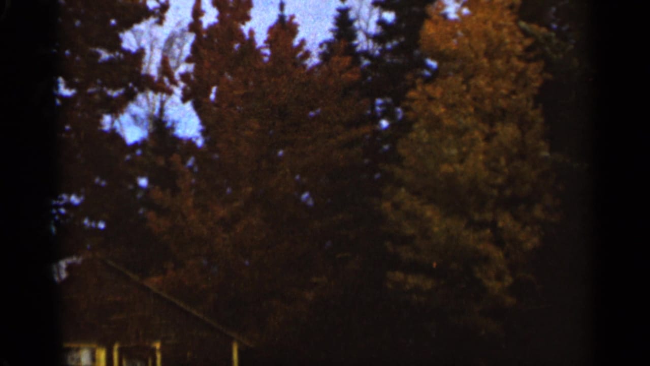 1965 Duluth 8mm frame showing tall autumn trees and a partial house roofline beneath dark film edges.