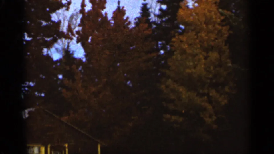 1965 Duluth 8mm frame showing tall autumn trees and a partial house roofline beneath dark film edges.