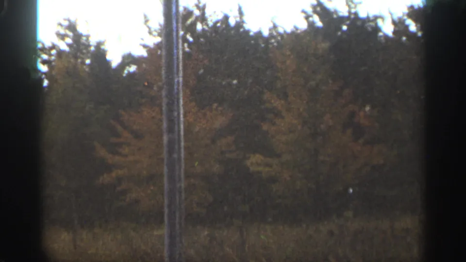 1965 Duluth-area 8mm frame showing a field and wooded autumn background with a foreground pole near center.