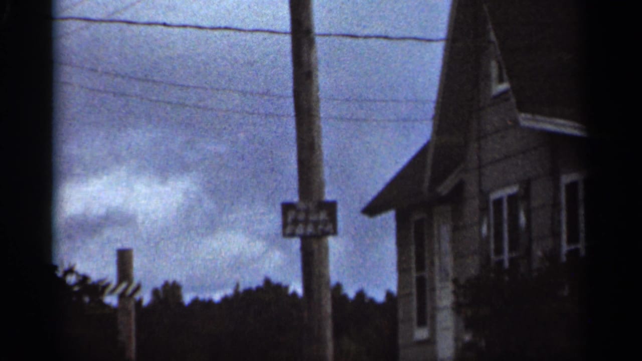 Telephone pole with a small sign beside a house and overhead wires.