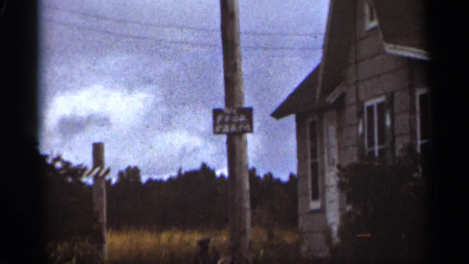 Duluth 1965 home-movie frame showing a posted sign on a utility pole beside a modest house exterior.