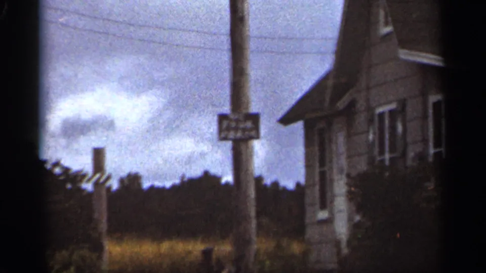 Final 1965 Duluth frame holding on a utility pole sign near a house, with field and treeline behind it.