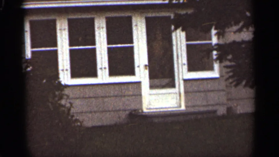 1965 Duluth exterior frame with the house front held in a soft, grainy 8mm view behind dark tree cover.