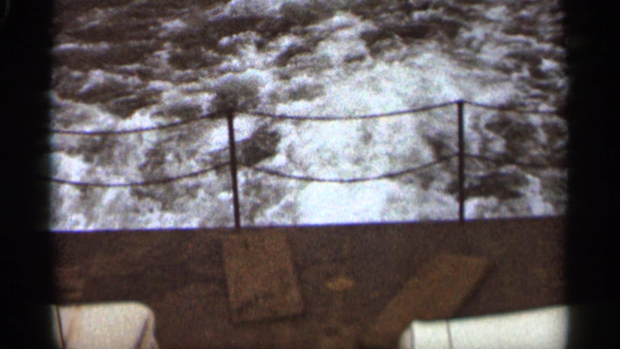 Foamy water seen past a rope railing at the stern of a moving boat.