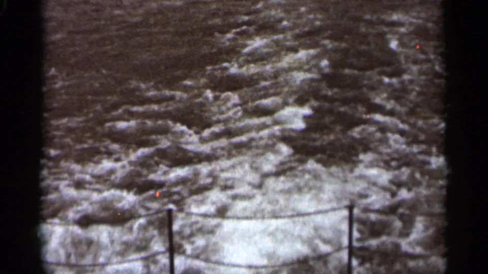 1965 Duluth 8mm frame with rough lake or river water beyond the stern rope rail of a moving boat.