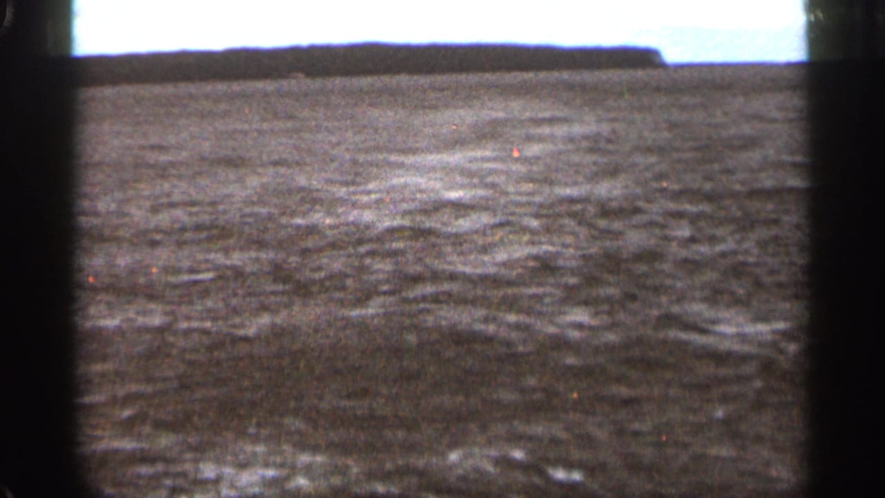 Choppy dark water beneath a pale sky, framed by black film borders.