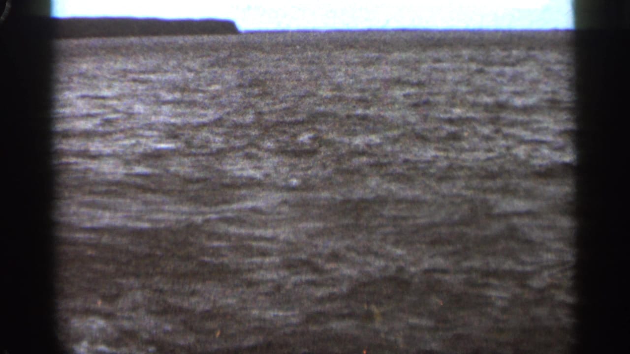 Textured waves and a flat horizon seen through dark vertical film borders.