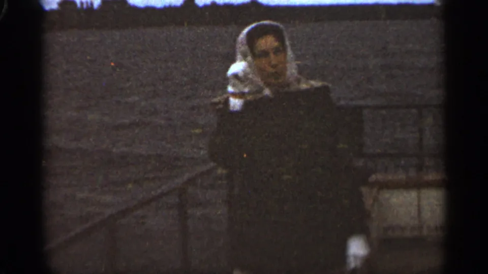 The woman remains near the railing in this Duluth 1965 home-movie frame, facing toward the camera against choppy water.