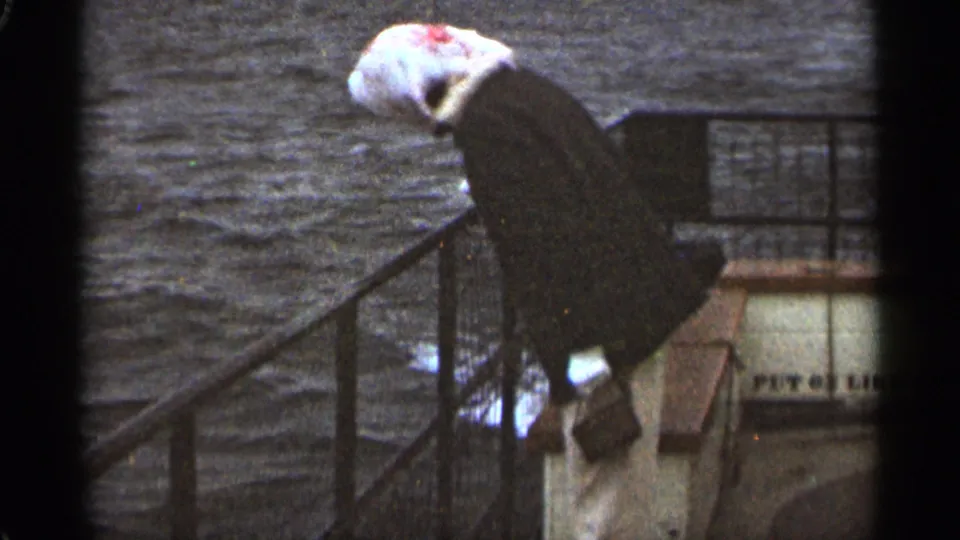 The woman turns downward by the metal railing, her white headscarf and gloves visible against the water in the 1965 Duluth footage.