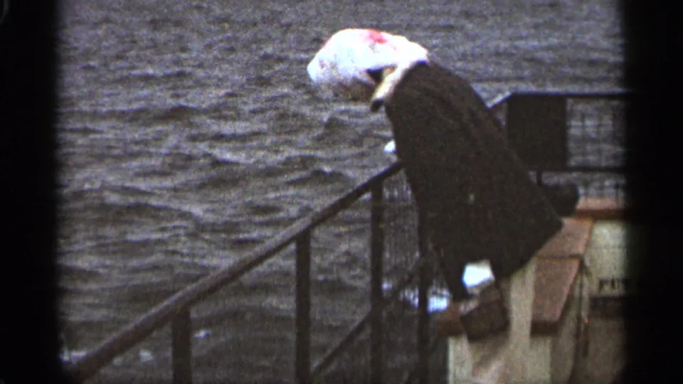 In 1965 Duluth home-movie footage, a woman in a headscarf and dark coat looks over a boat edge toward the water.