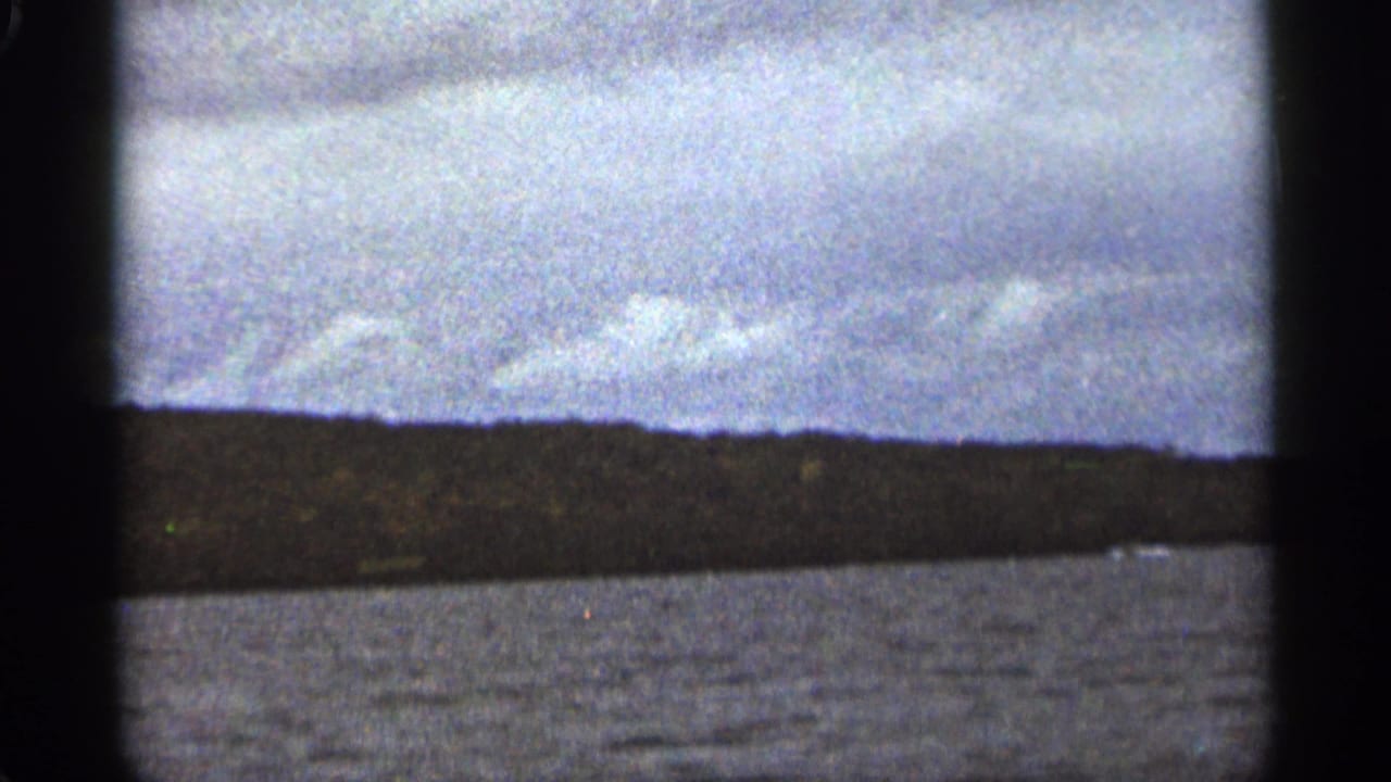 A handheld 8mm view shows rippled water and a distant shoreline under a cloudy sky near Duluth, Minnesota.