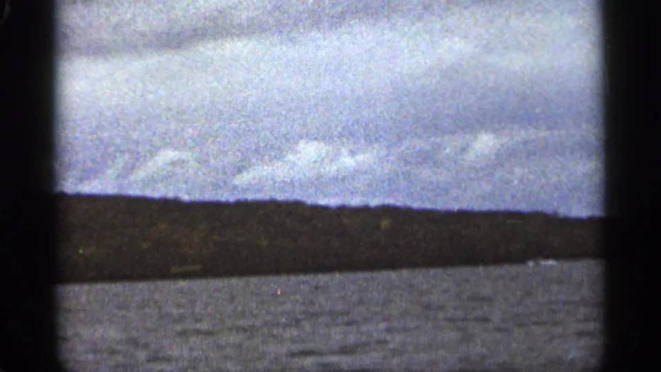 A handheld 8mm view shows rippled water and a distant shoreline under a cloudy sky near Duluth, Minnesota.
