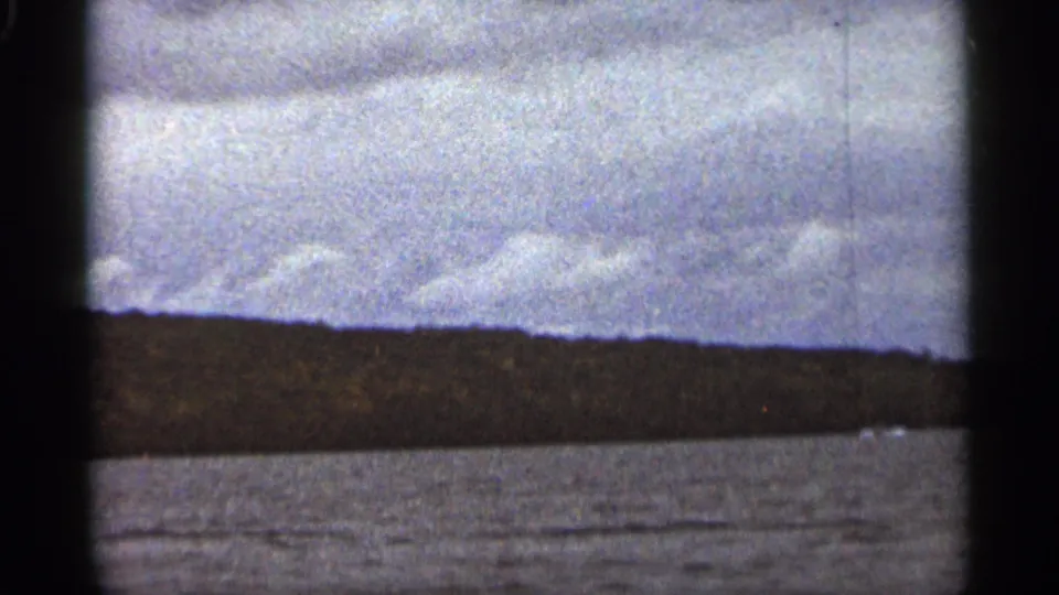 The 1965 Duluth boat view continues across open water toward a low shoreline, with clouds and 8mm grain visible.
