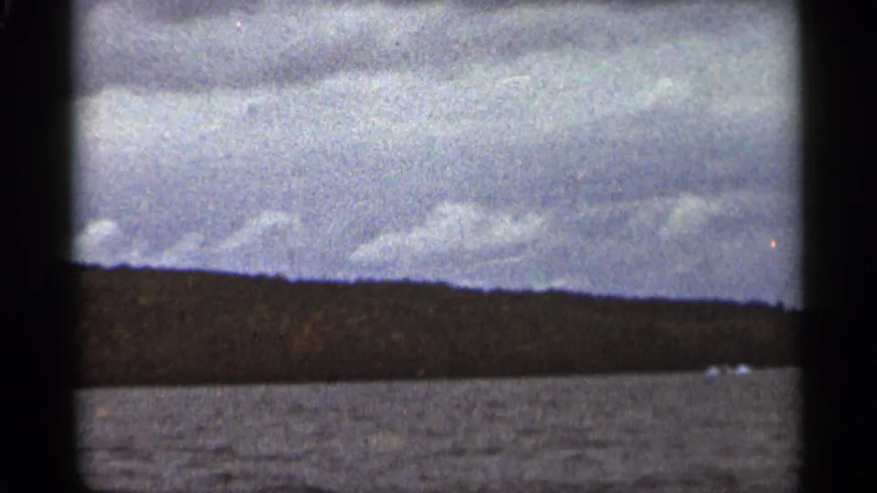 A grainy 8mm frame shows open water and a distant Duluth shoreline beneath a gray, clouded sky.