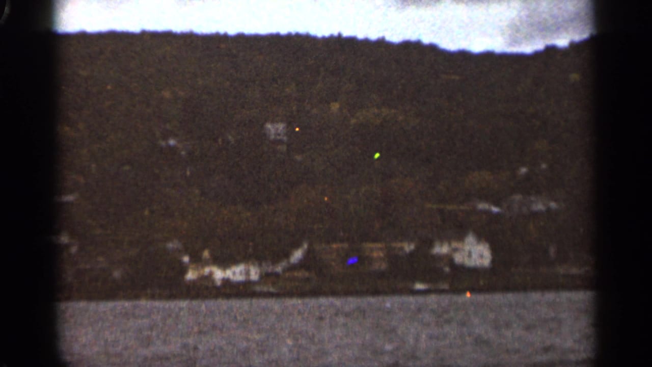 Wide lakeside view with dark treeline, pale buildings, and water in the foreground.