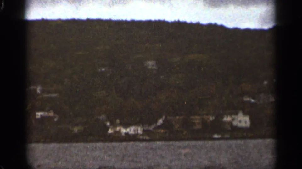 Grainy 1965 Duluth 8mm frame holding on open water, a distant treeline, and pale structures along the shore.