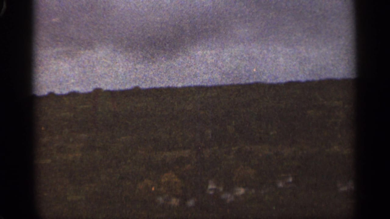 Dark tree-covered ridge beneath a cloudy sky, with faint structures near the lower edge.