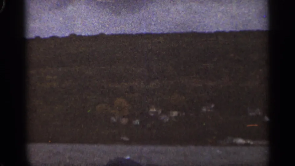 Underexposed 1965 Duluth landscape frame with a broad dark hillside, cloudy sky, and indistinct structures or shoreline details below.