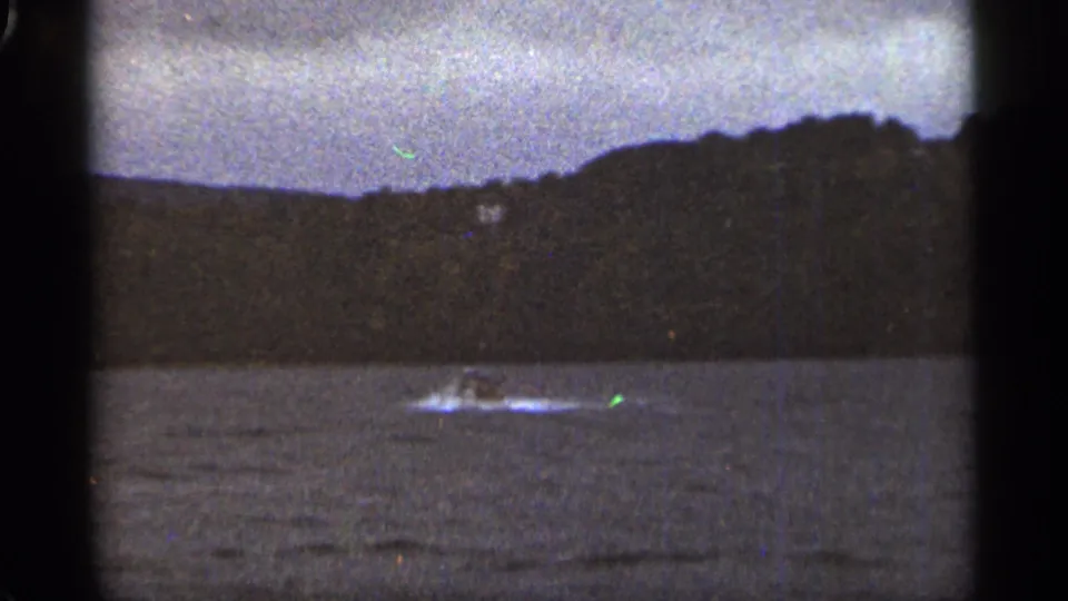 The view shifts to open water near a dark shoreline in the Duluth-area footage, with a small distant craft or wake crossing the frame.