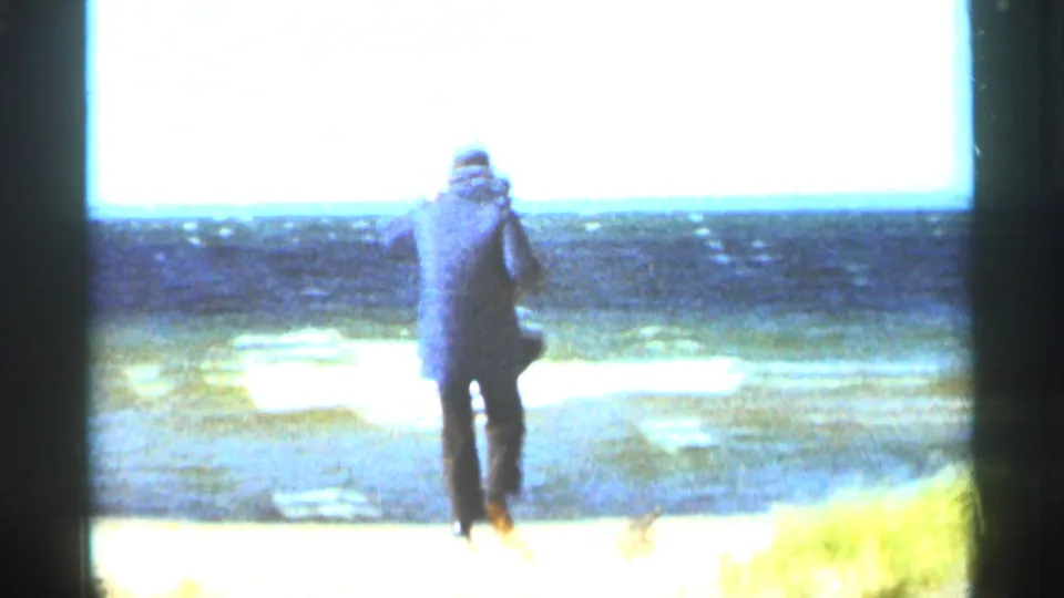A warmly dressed man walks across a sandy Duluth beach toward choppy water in 1965 home-movie footage.