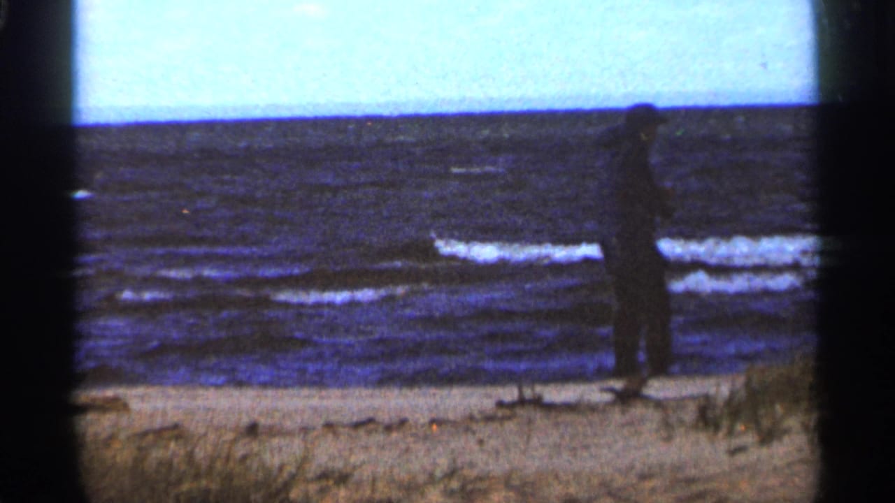 Distant man standing near the waterline on a windswept beach.