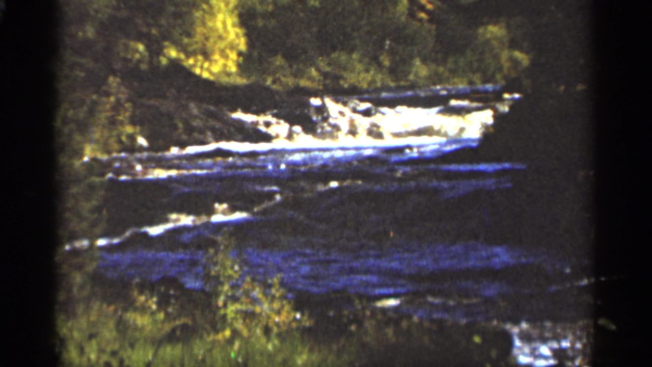 Swift river water flowing over rocks with wooded banks and film gate edges visible.