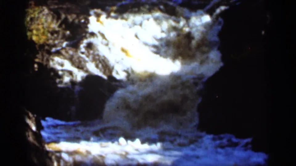 1965 Duluth frame showing a close view of bright white water flowing across rocks, with deep surrounding shadow.