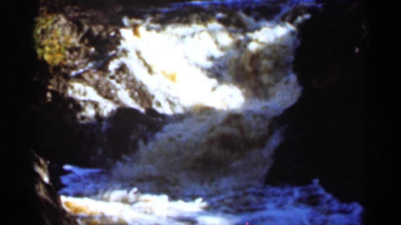 Waterfall rushing over dark rocks into a foamy riverbed.