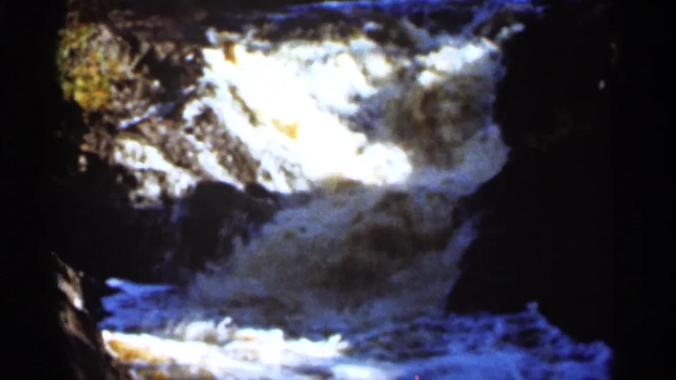 1965 Duluth home-movie frame showing water dropping through dark rocks into frothy white spray.