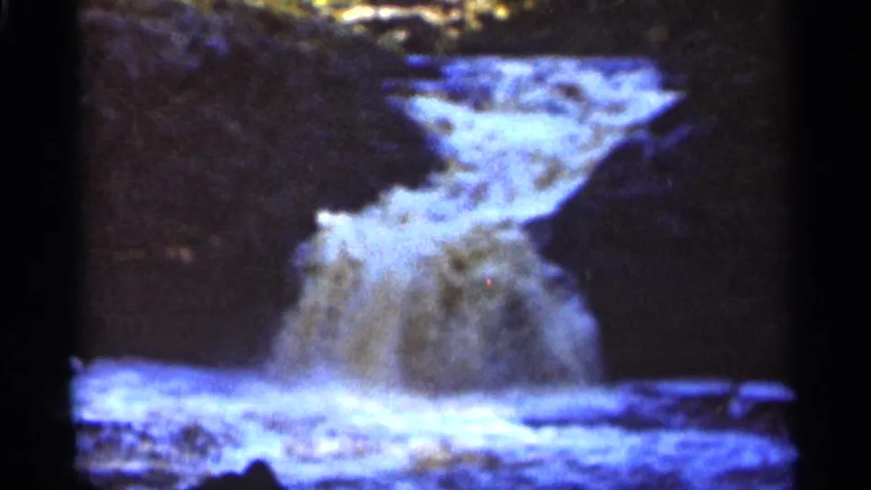 1965 Duluth 8mm frame with turbulent waterfall spray below a dark rock ledge and bright water surface.