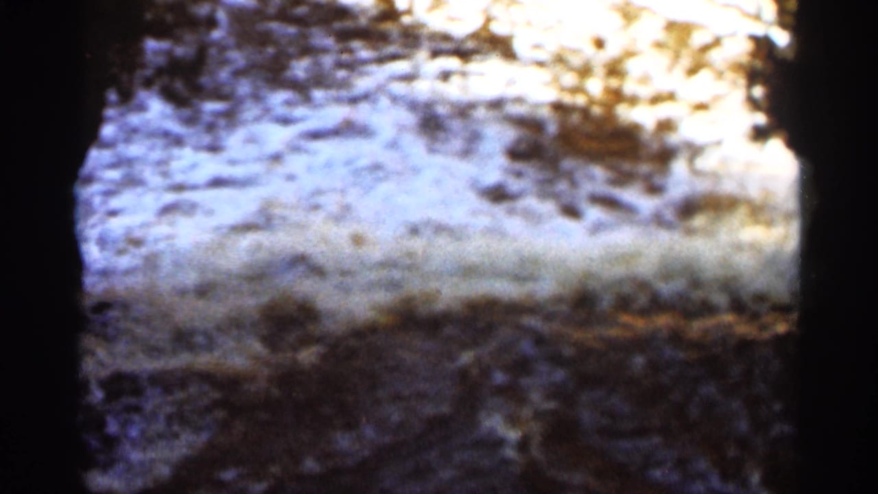 Shallow stream surface with glare, rocks, and dark vertical frame edge.