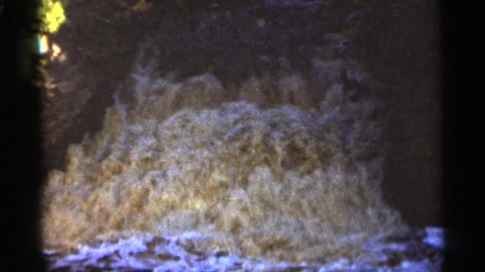 1965 Duluth 8mm frame showing pale cascading water in the lower half, with darkness, foliage, and visible film wear above.