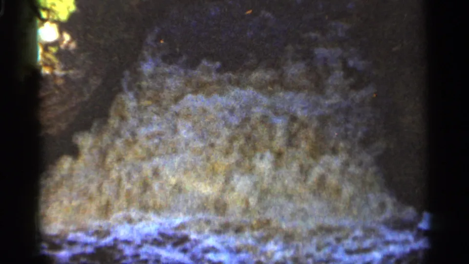 1965 Duluth frame of a dim waterfall or fountain cascade, with blue highlights, heavy grain, and dark surrounding forms.