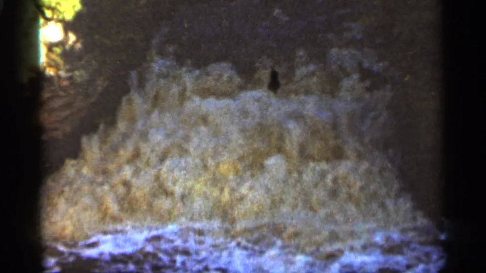 Turbulent water spills across dark shoreline rocks in Duluth, Minnesota archival 8mm footage from 1965.