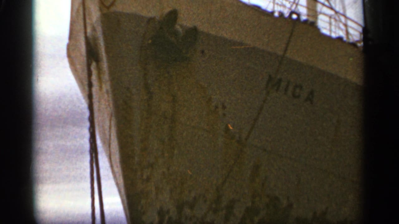 Close view of a ship bow with Mica lettering and dark rigging lines in front.