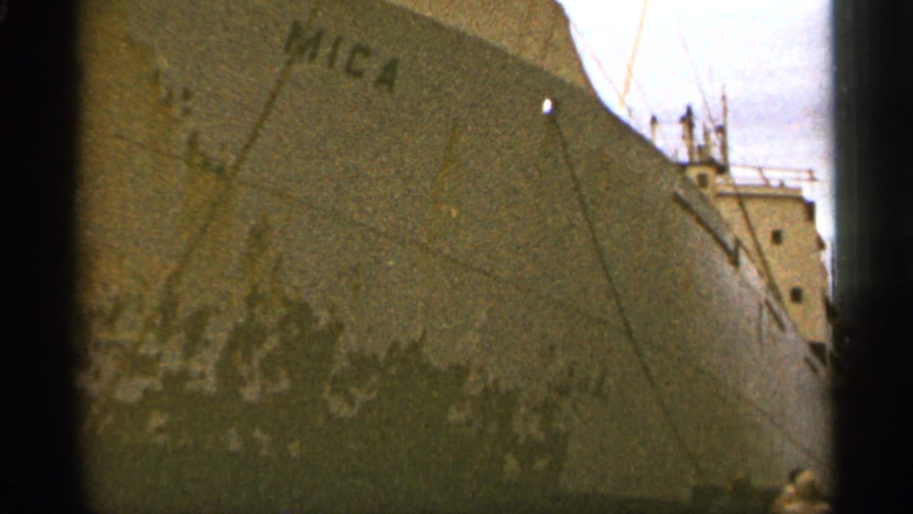 Close view of the MICA cargo ship hull at a dock with rigging and small figures below.