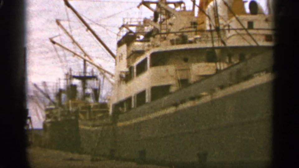 Duluth port scene from 1965 with moored cargo ships, cranes, rigging, and a dark film-frame edge from the 8mm scan.