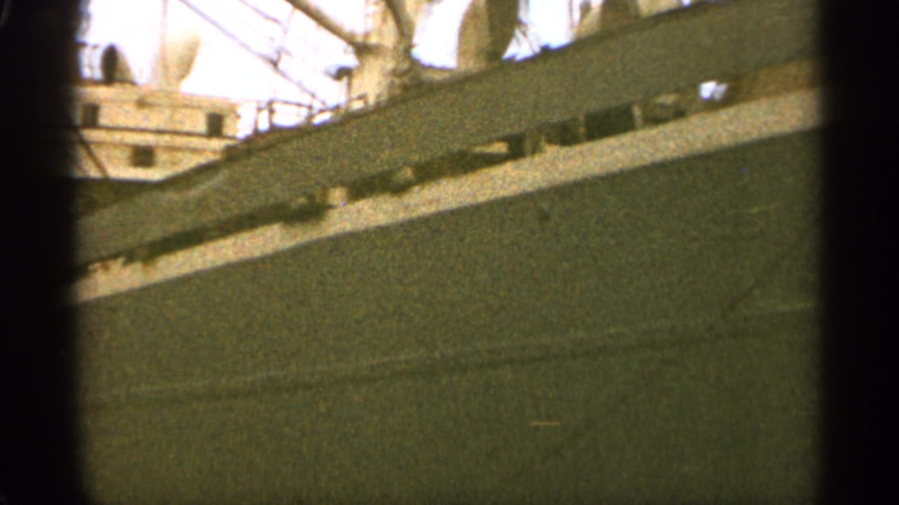 Close view along a ship's dark hull with railings and upper deck details above.