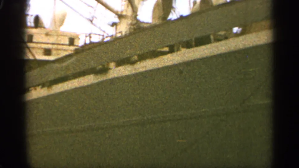 1965 Duluth footage frame looking along the side of a large moored ship, with railings and deck equipment visible above the hull.