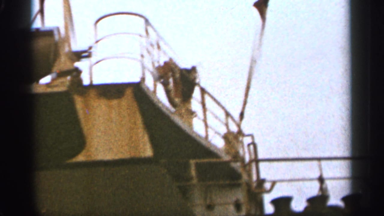Upper deck area of a large ship with railings, rigging, and bright sky behind it.