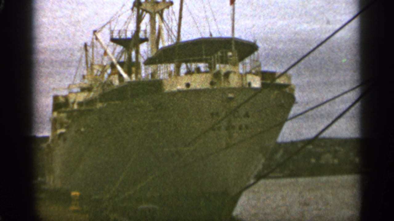 Bow of a large docked cargo ship with rigging and mooring lines visible.