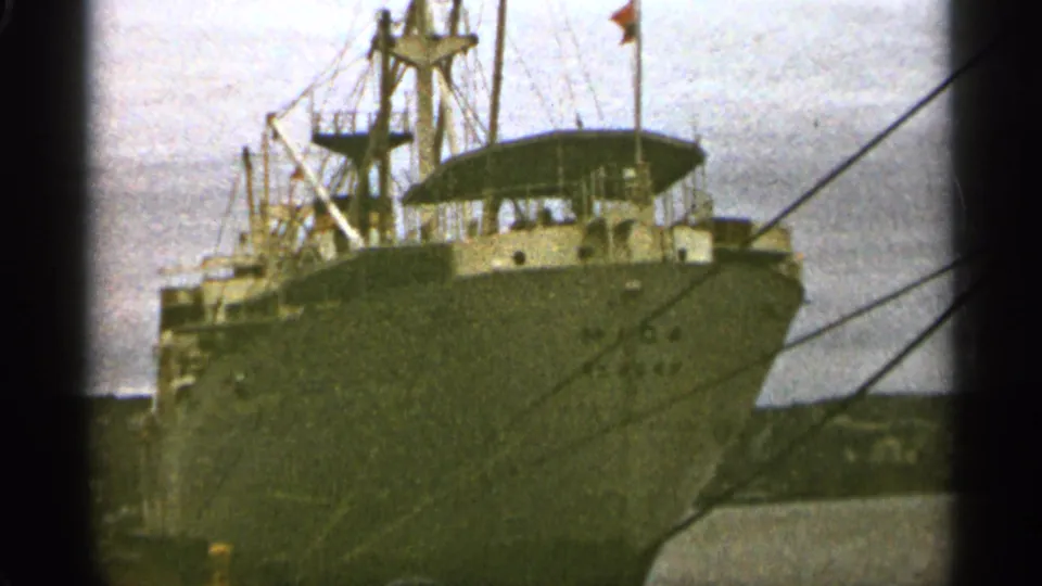 Home-movie view of a large cargo ship bow in Duluth harbor, with rigging and mooring lines crossing the soft 8mm frame.