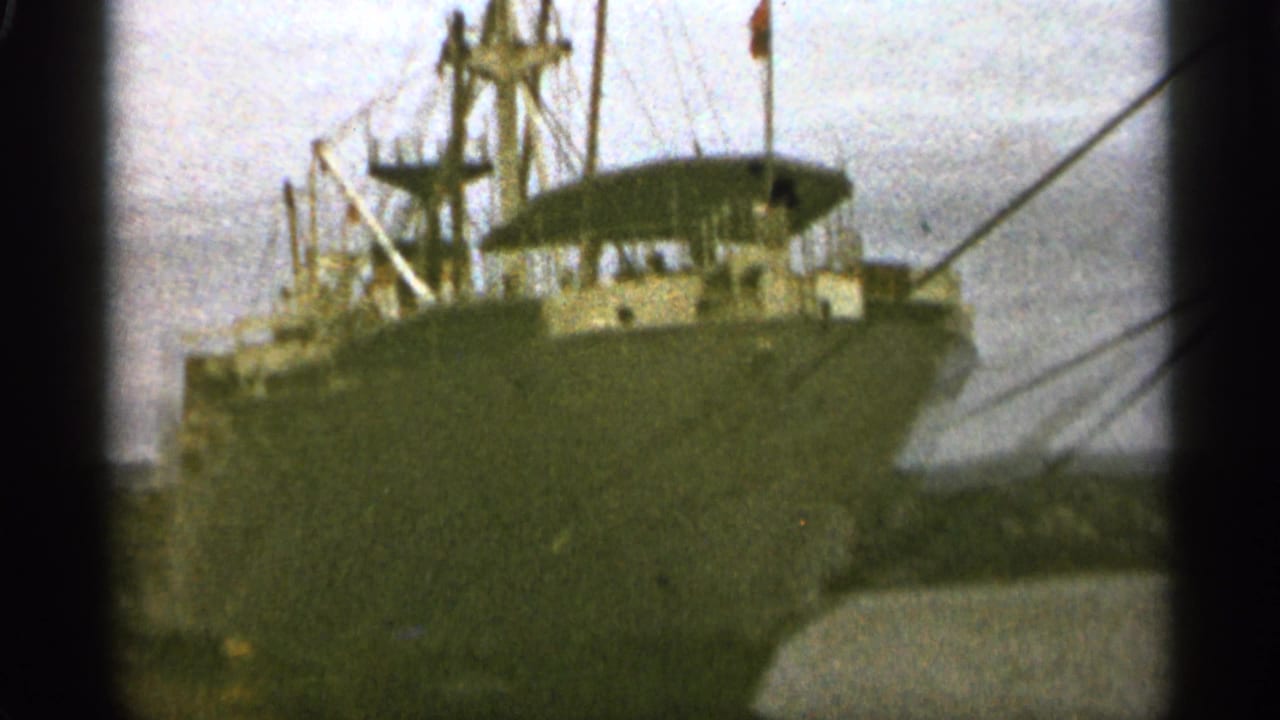 Cargo ship docked near water with film-frame borders visible.
