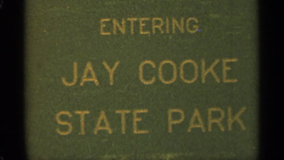 Close 1965 Minnesota travel frame of a green sign reading ENTERING JAY COOKE STATE PARK in yellow lettering.