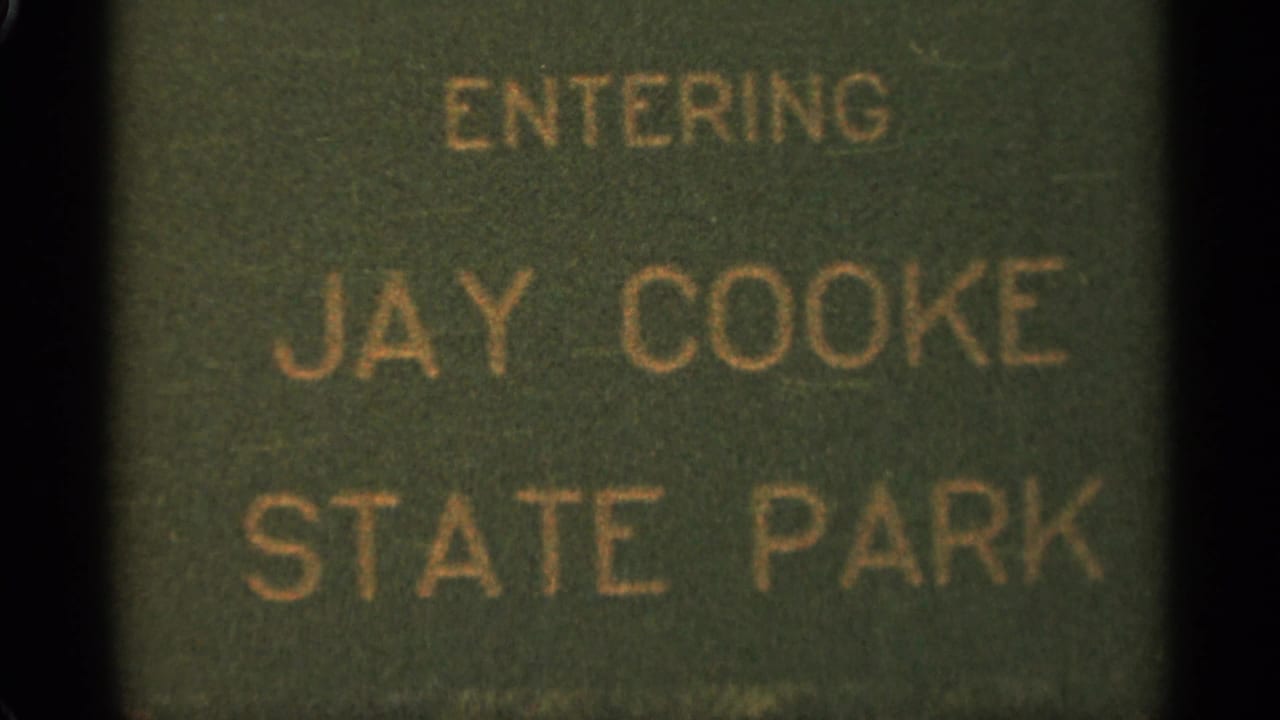 Green Jay Cooke State Park sign seen in soft focus with dark film border.