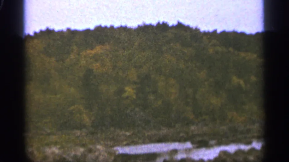 1965 Duluth-area 8mm frame showing a wooded shoreline or hillside with water under a soft sky.